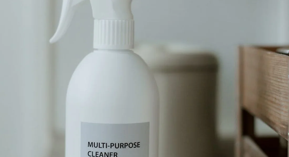 Close-up of a white spray bottle labeled 'MULTI-PURPOSE CLEANER' with a guinea pig cage visible in the background.