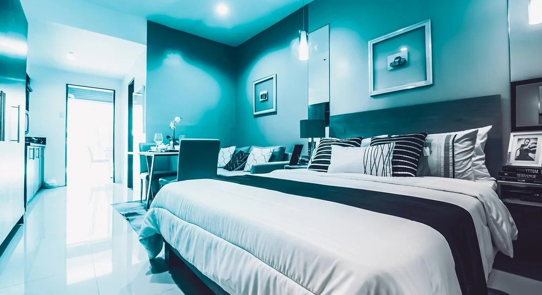 Blue-tinted modern bedroom with a large bed featuring layered white and dark bedding and several pillows.