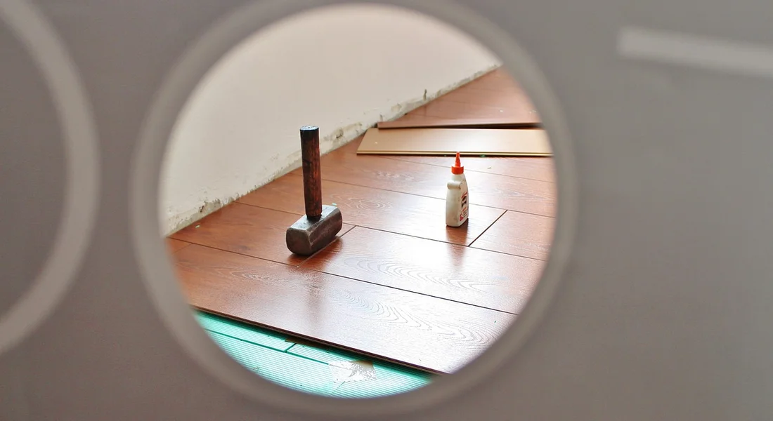 Hammer and a bottle of glue on a wooden floor seen through a circular hole, illustrating a DIY decision point.