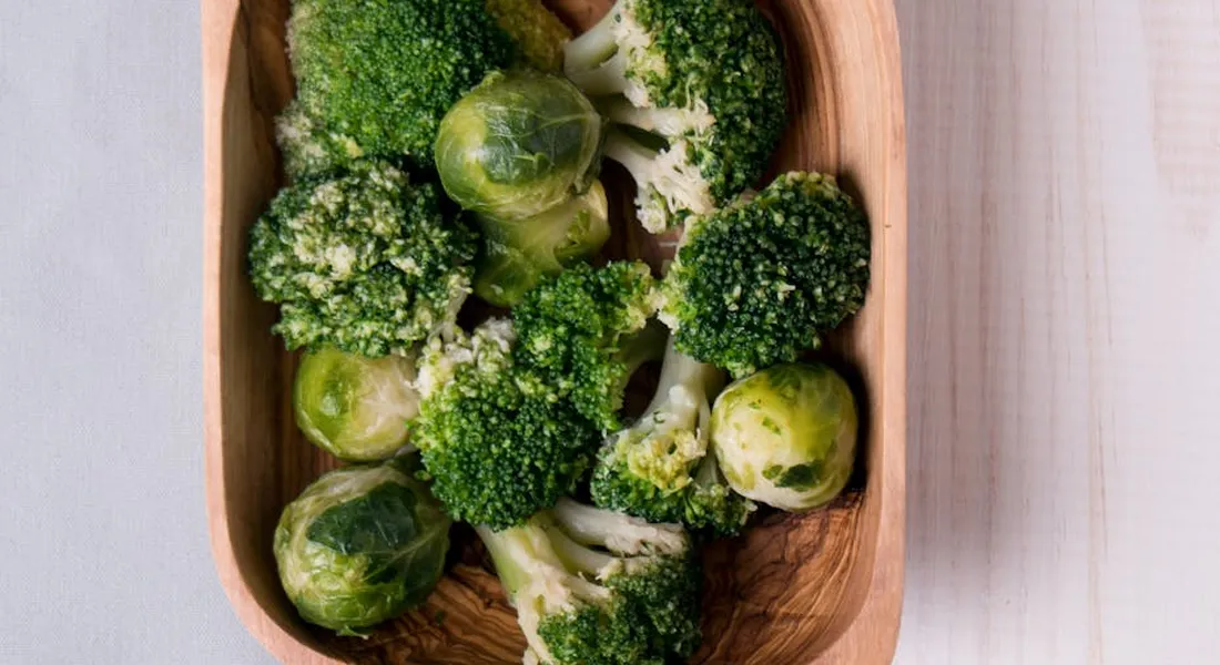Wooden bowl filled with broccoli florets on a pale wooden surface