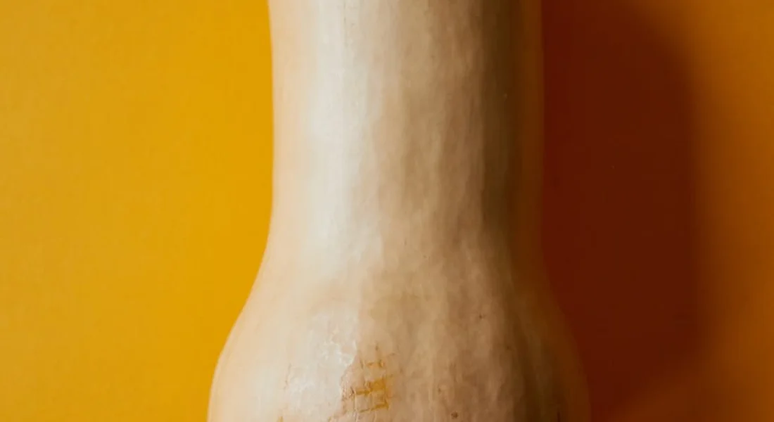 Close-up of a butternut squash neck against a warm orange background.