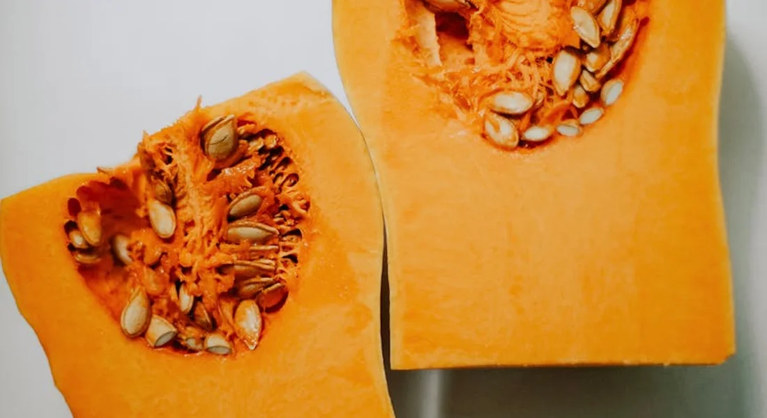 Two halves of vibrant orange butternut squash with seeds visible against a light background.