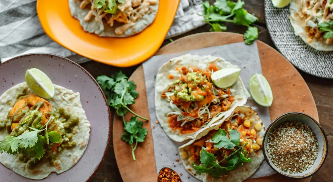 Plates of tacos with fresh cilantro garnish and lime wedges on a wooden board.