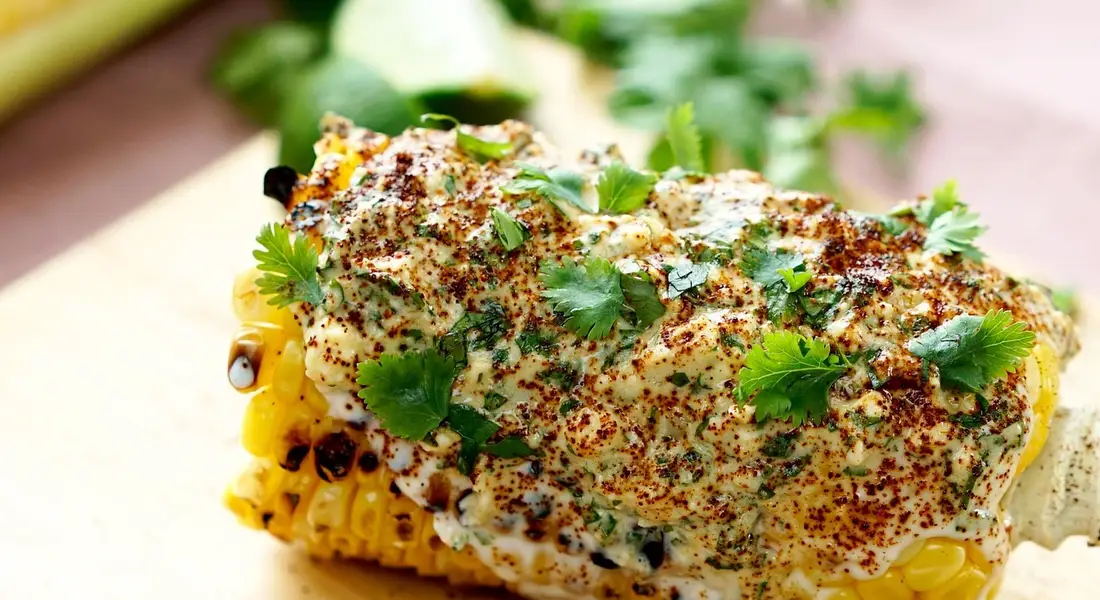 Close-up of corn on the cob topped with a creamy sauce and fresh cilantro garnish.