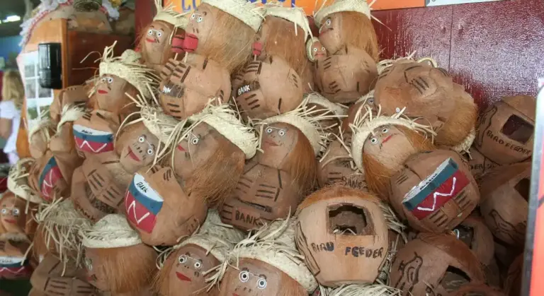 A large pile of carved coconut shells, some with painted faces and straw hair, stacked together in a decorative display.