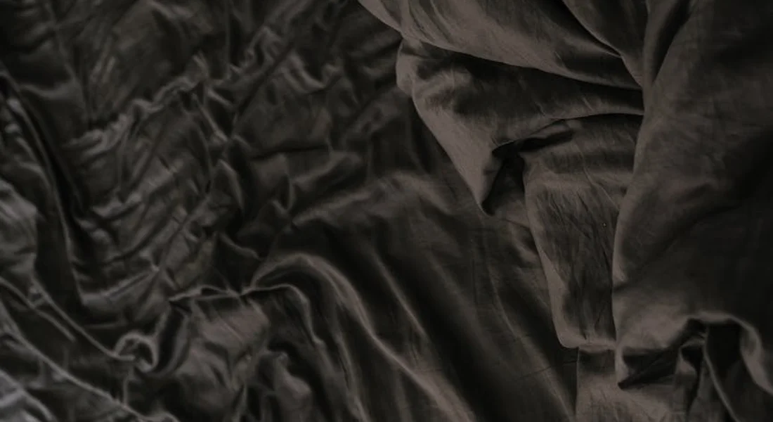 Close-up of dark, wrinkled fabric acting as bedding backdrop