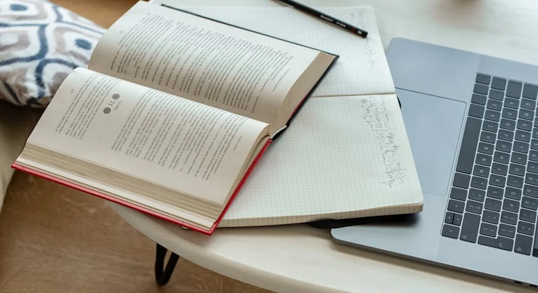 Open book and notebook on a table with a laptop nearby, illustrating research and planning for a hypoallergenic setup for humans and guinea pigs.