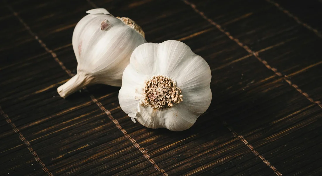 Two garlic bulbs on a dark woven surface