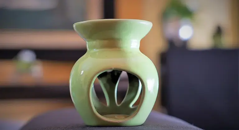 Green ceramic essential oil diffuser with vent openings, resting on a dark surface