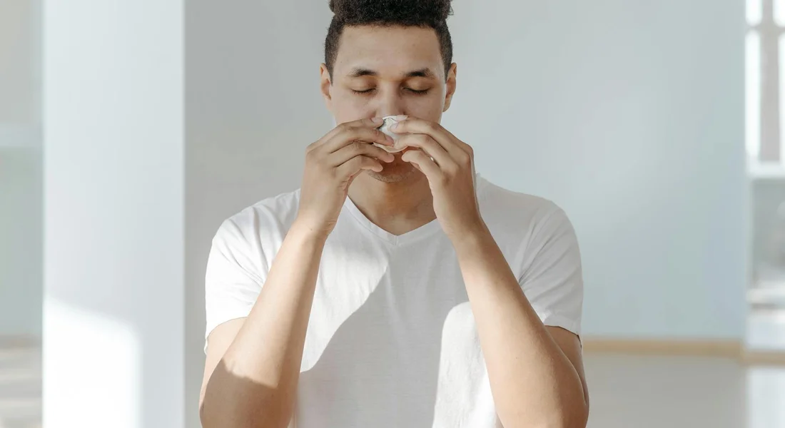 A person sneezing into a tissue, illustrating allergy symptoms