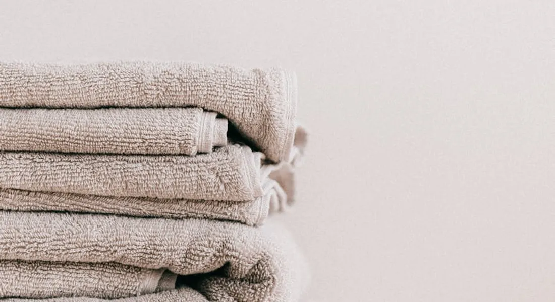 Stack of folded beige towels against a pale background.