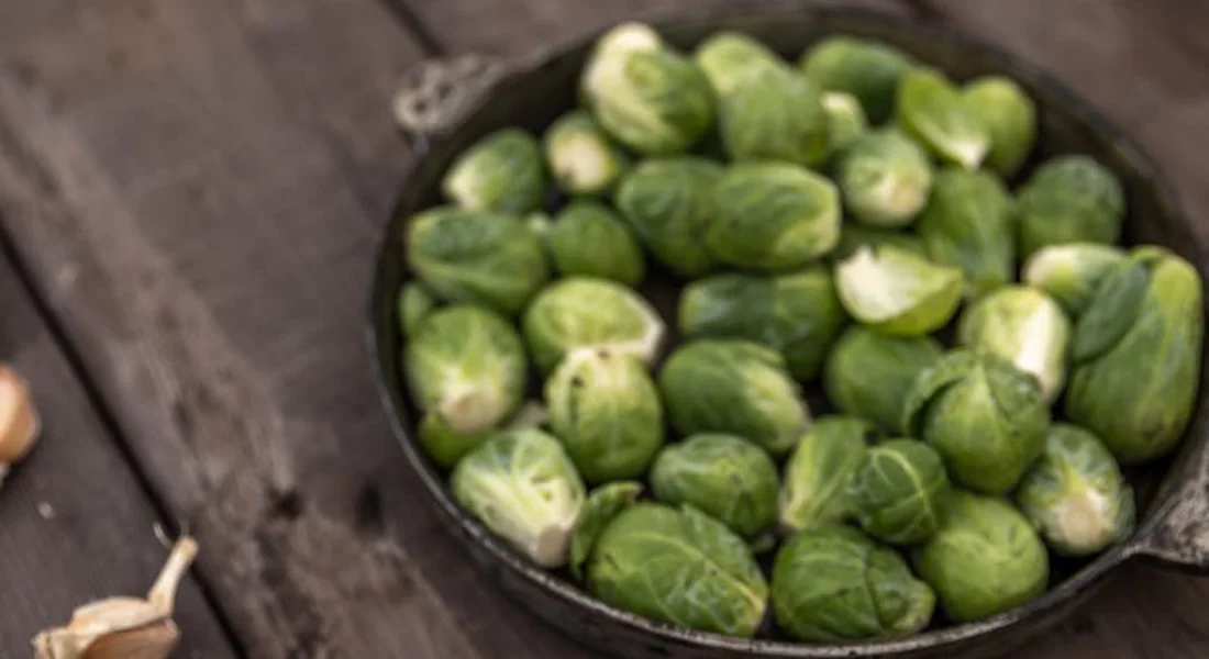Brussels sprouts in a skillet on a rustic wooden surface, ready to be prepared as a treat for a guinea pig