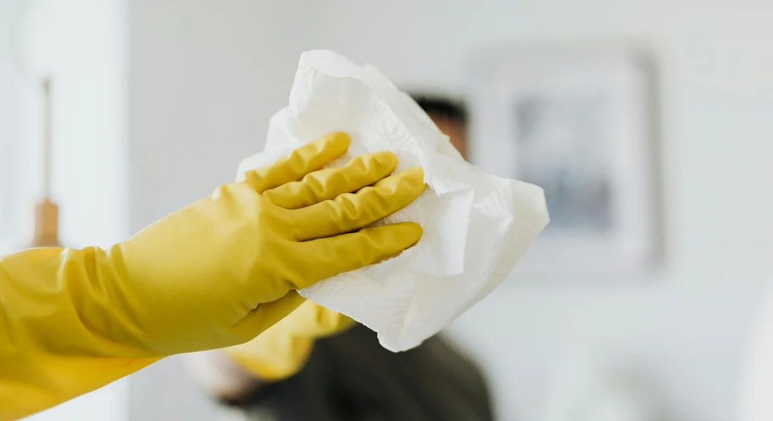 A gloved hand holding a white cleaning cloth, wiping a surface.