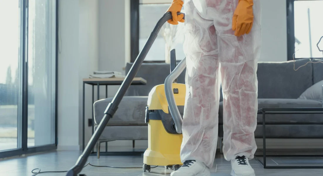 A person in protective cleaning gear vacuums a modern living space, illustrating cleaning practices for maintaining guinea pig habitats.
