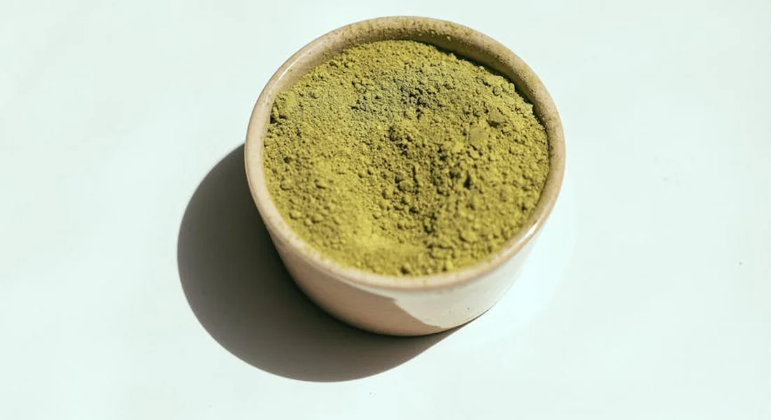 Small beige ceramic bowl filled with green powder on a light surface, casting a shadow.