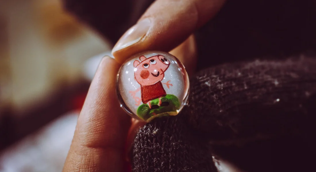 Close-up of a round badge featuring a cartoon pig held by a finger, with a guinea pig's fur in the background