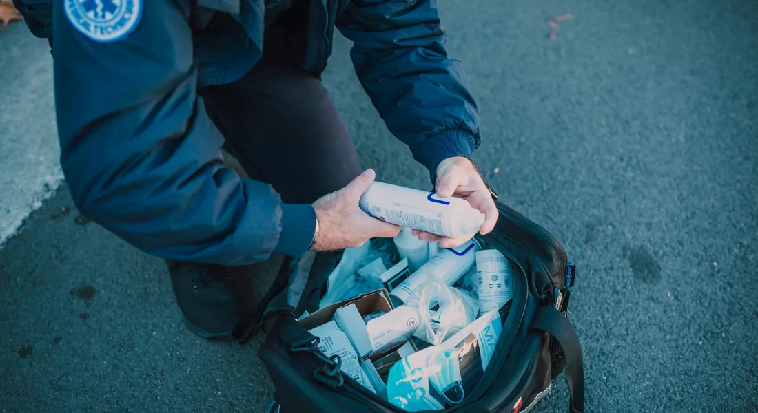 Person in a blue jacket organizing a first aid supply bag with assorted items on a paved surface