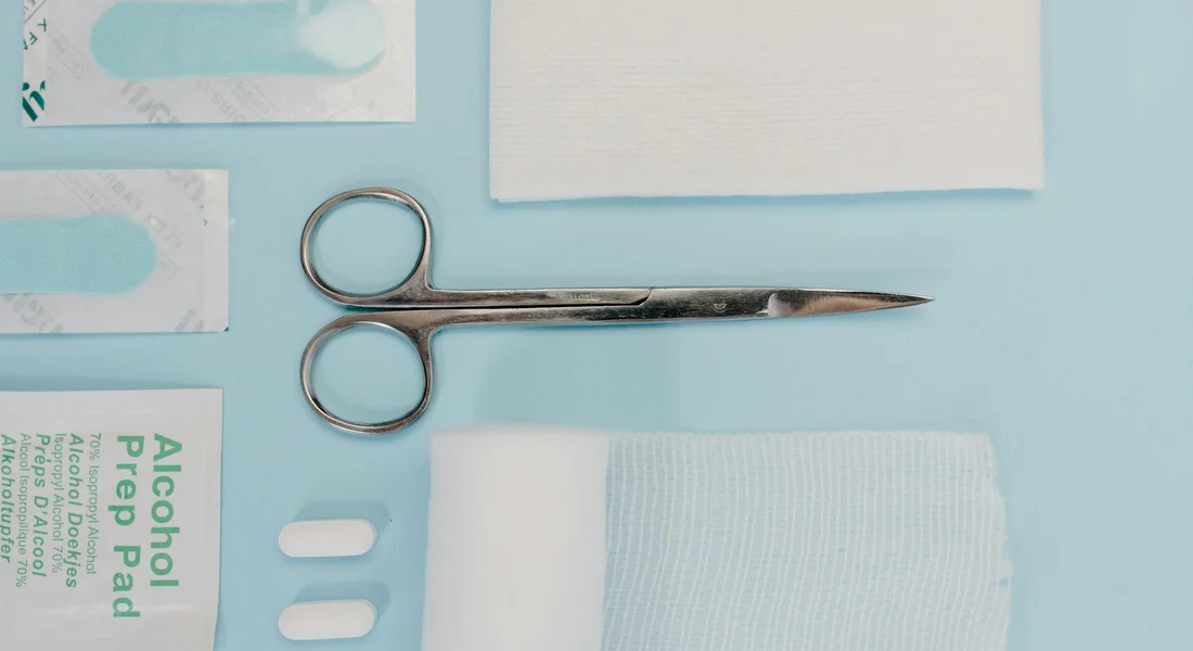 Flat lay of guinea pig first aid supplies on a light blue background, including scissors, alcohol prep pads, gauze, and small medical items.