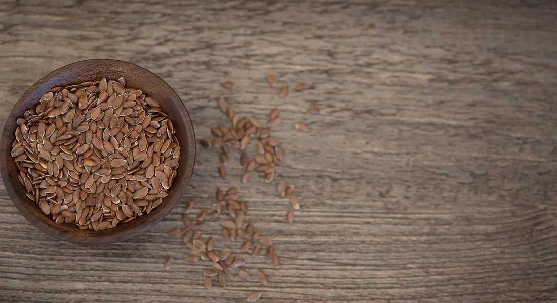 Round wooden bowl filled with guinea pig seeds on a rustic wooden surface, with some seeds scattered nearby