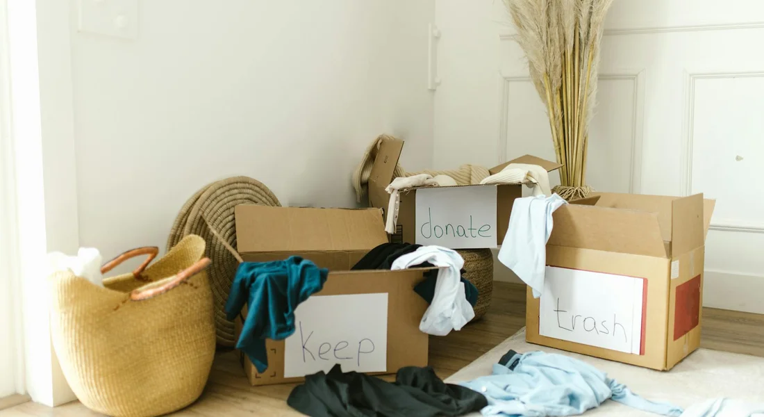 Room with several labeled cardboard boxes (Donate, Keep, Trash) and clothing items, illustrating sorting and organizing supplies.