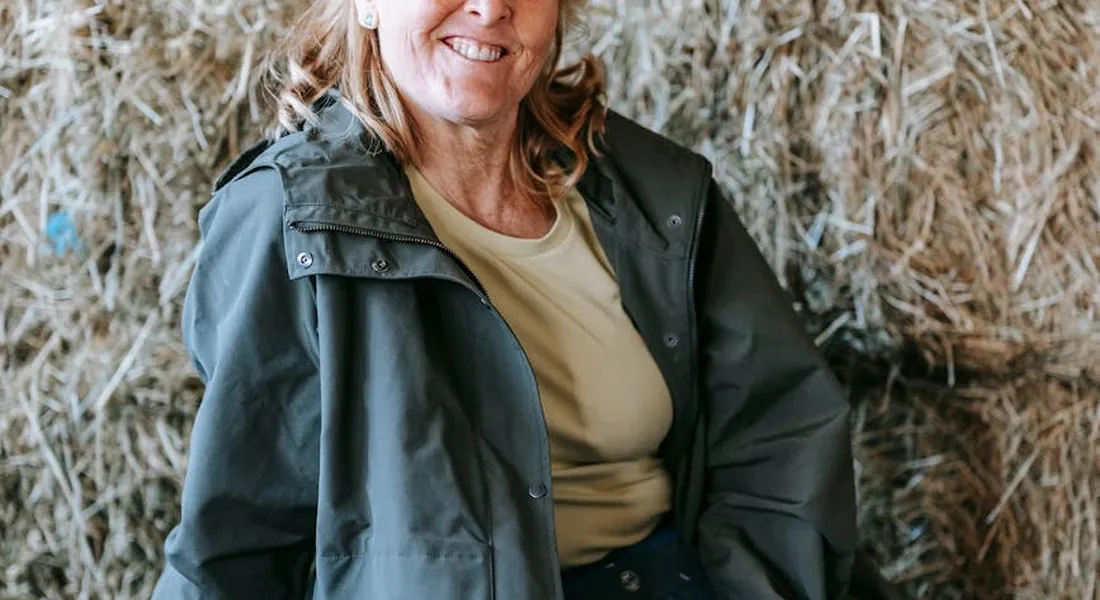 Person in a green jacket standing in front of stacked hay bales in a barn, illustrating hay storage.