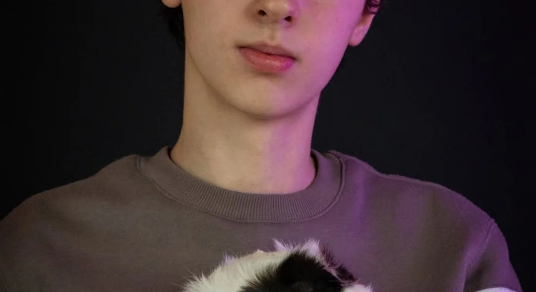 Person holding a guinea pig close to their chest, with soft purple lighting.