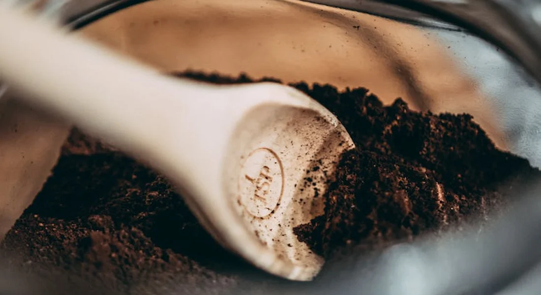Close-up of a white scoop resting in a jar of dark brown pellet crumble, illustrating storage considerations for freshness.