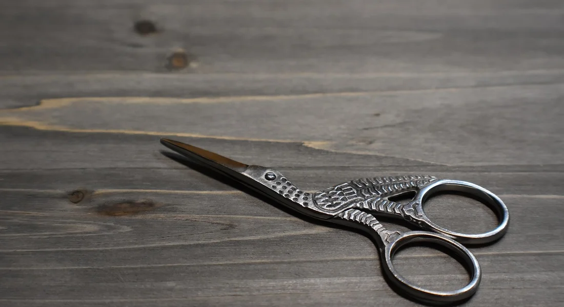 Small grooming scissors resting on a dark wooden surface.