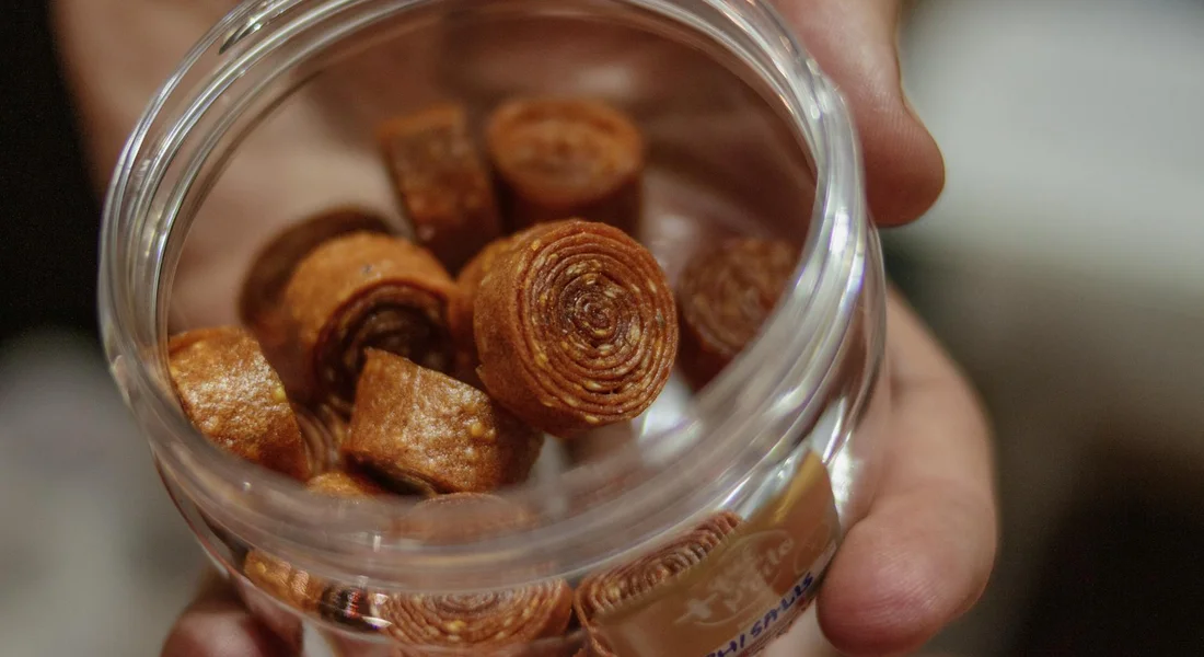 Close-up of a hand holding a glass jar filled with round, dried training treats for guinea pigs.