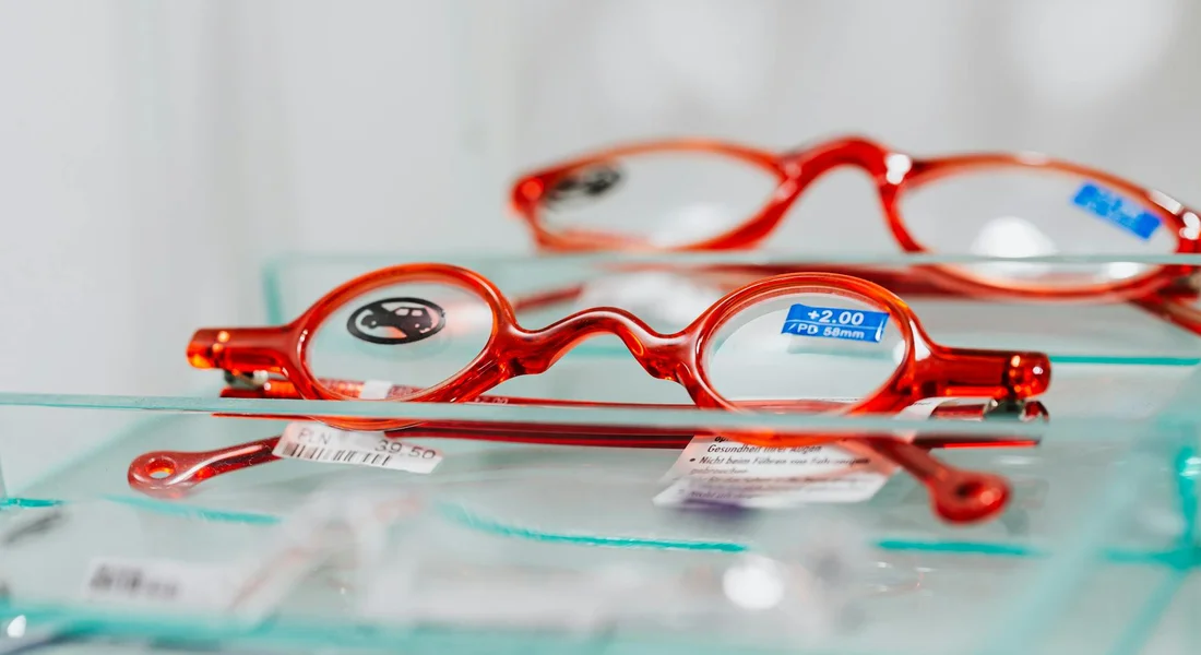 Close-up of red eyeglasses resting on a glass surface, illustrating vision and eye anatomy concepts.