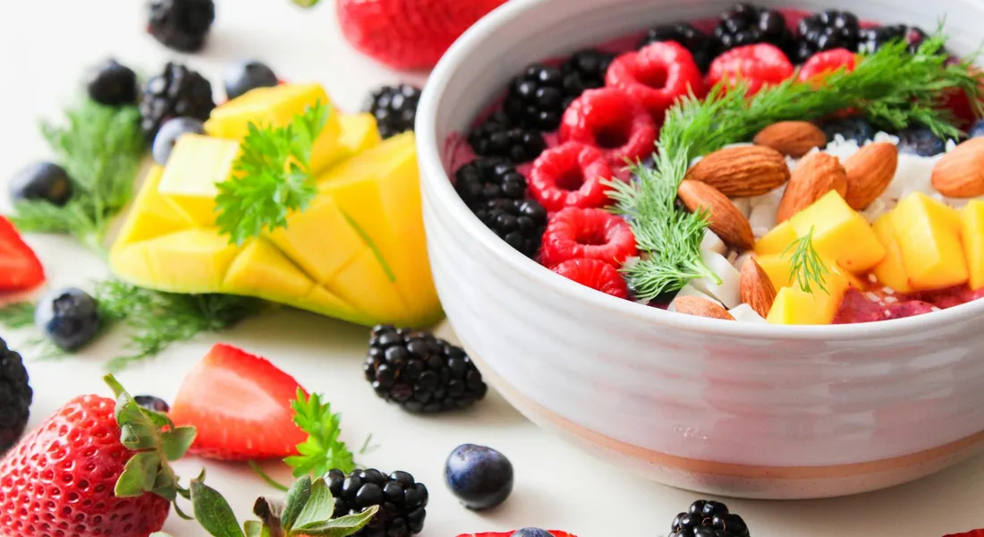 Colorful bowl of mixed fruits and berries with fresh herbs on a light surface, illustrating vitamin C-rich snacks for guinea pigs.
