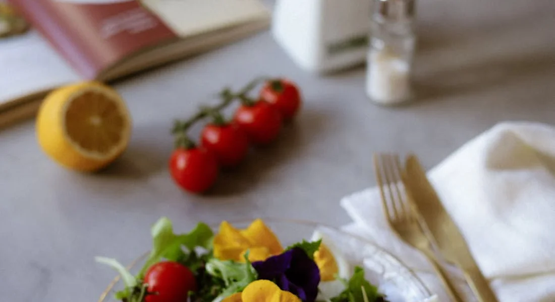 Blurred image of a fresh salad with arugula, cherry tomatoes, and lemon on a table with a fork and napkin.