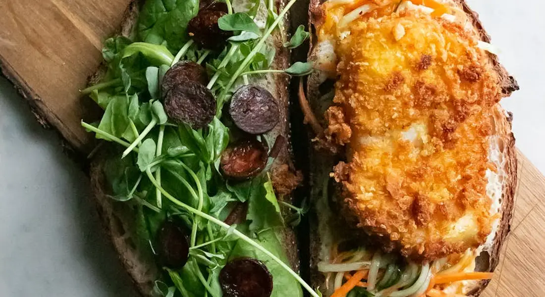 Open-faced bread topped with arugula greens and small round olives on one half, plus a golden-brown breaded croquette on the other half.