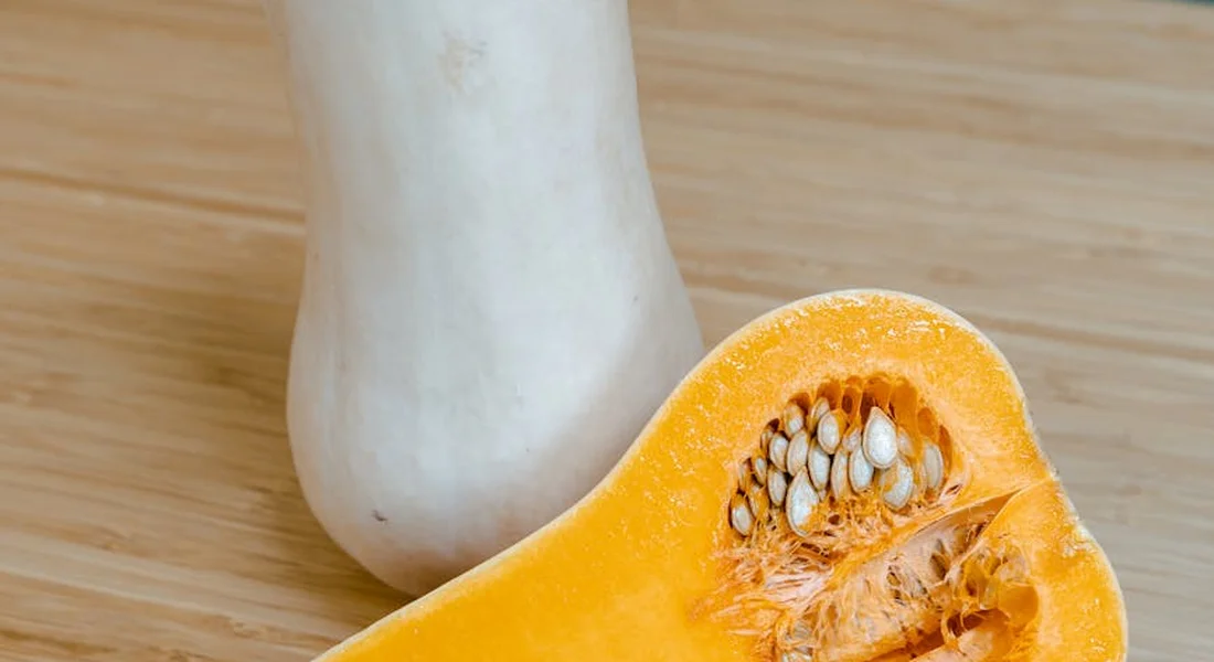Half-cut butternut squash with exposed seeds on a wooden surface.