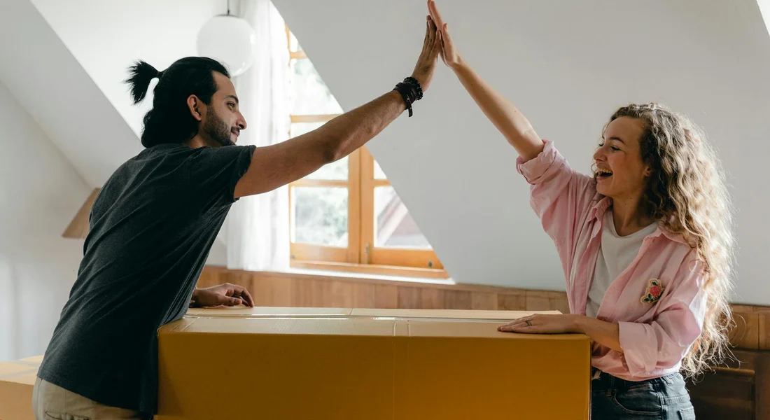 Two people high-fiving over a large cardboard box in a bright room, illustrating cardboard play opportunities.