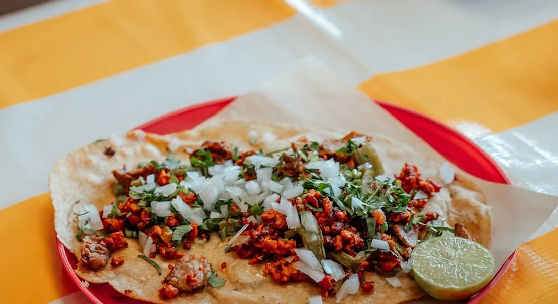 Plate with a tortilla topped with chopped cilantro, onions, and meat crumbles, with a lime wedge on a red plate