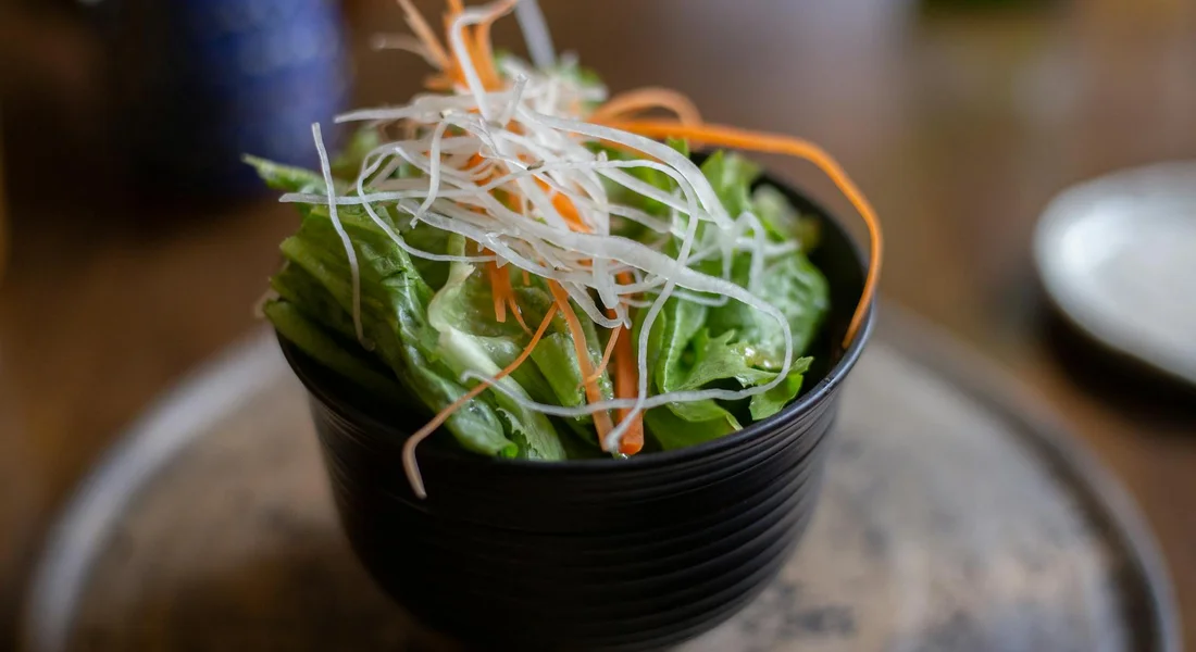 A bowl of fresh mixed greens topped with thinly shredded daikon radish and carrot ribbons.