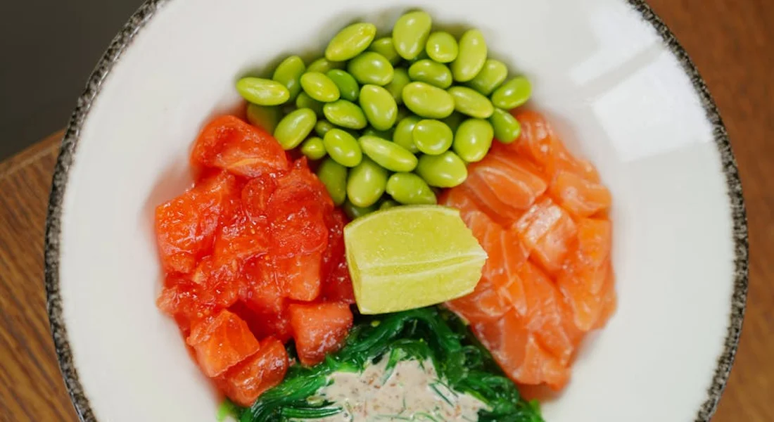 Bowl with edamame pods, diced tomatoes, greens, and a lime wedge