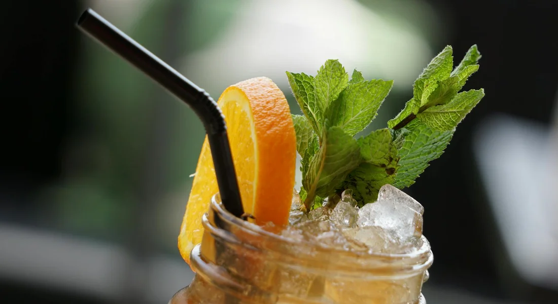 Fresh mint leaves and an orange slice garnish a mason jar with a black straw
