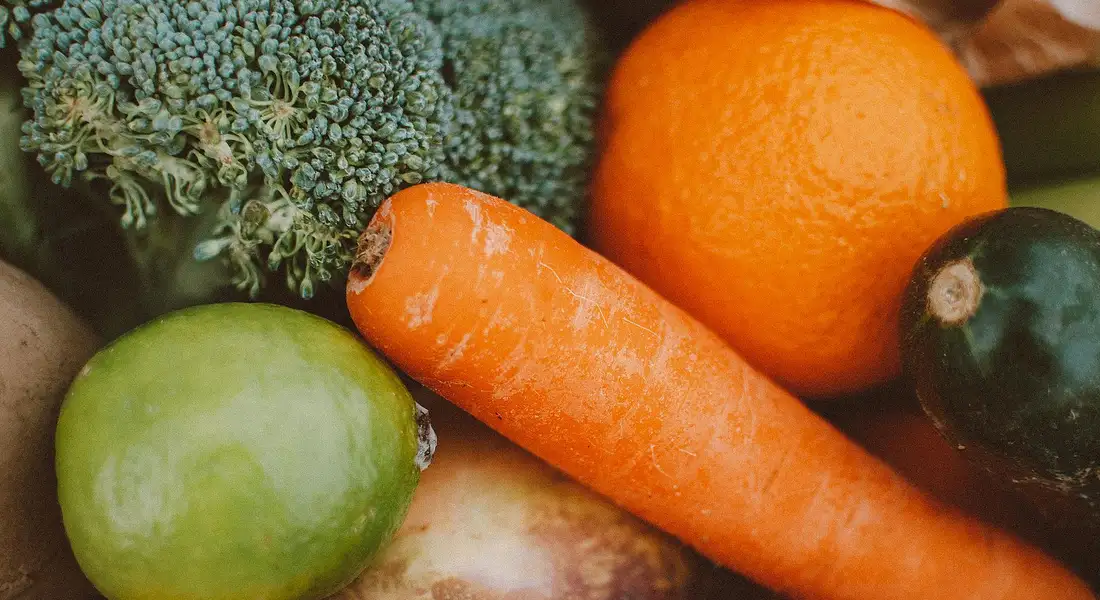 A colorful assortment of fresh vegetables including broccoli, a carrot, an orange, and a green fruit arranged together