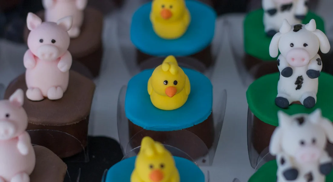 Close-up of bite-sized desserts with bright fondant animal toppers, including yellow ducks and pink pigs, arranged on colorful bases.