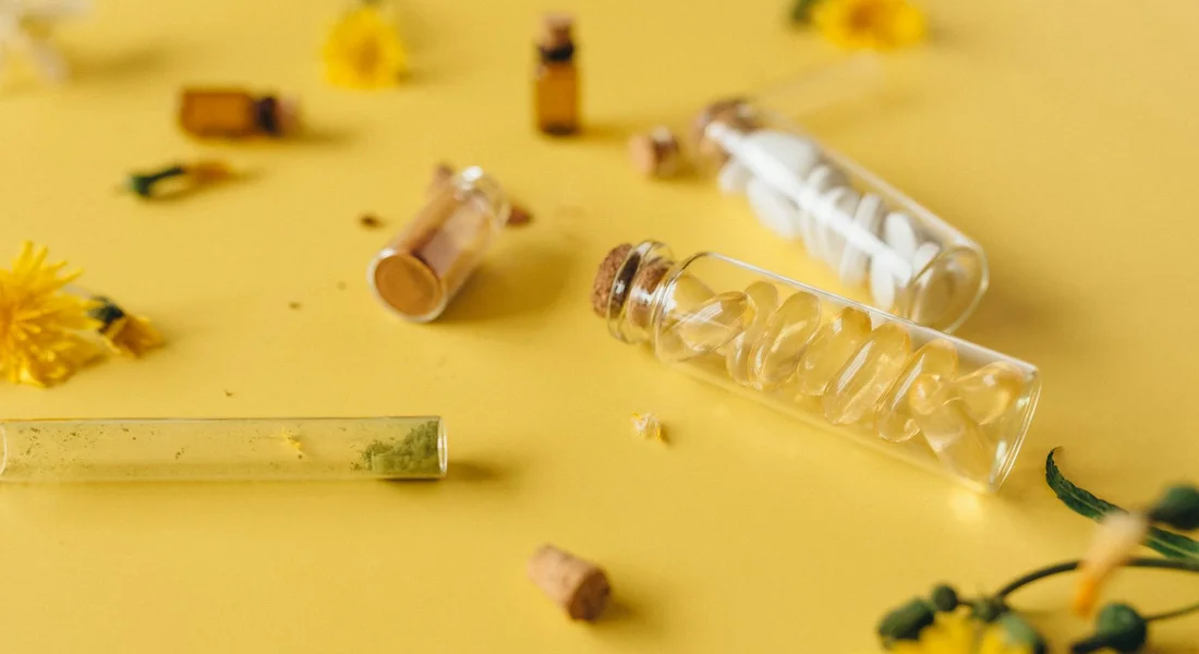 Small glass vials on a yellow background with scattered plant matter, representing vitamin supplements for small pets.