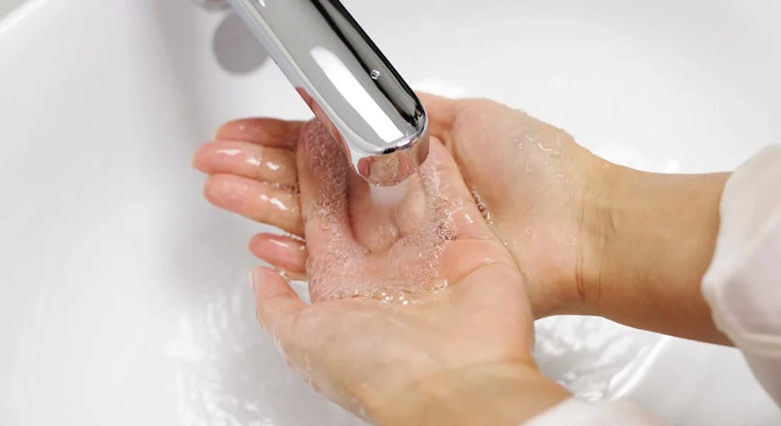 Close-up of hands under running water in a sink, illustrating hygiene before cleaning a guinea pig cage