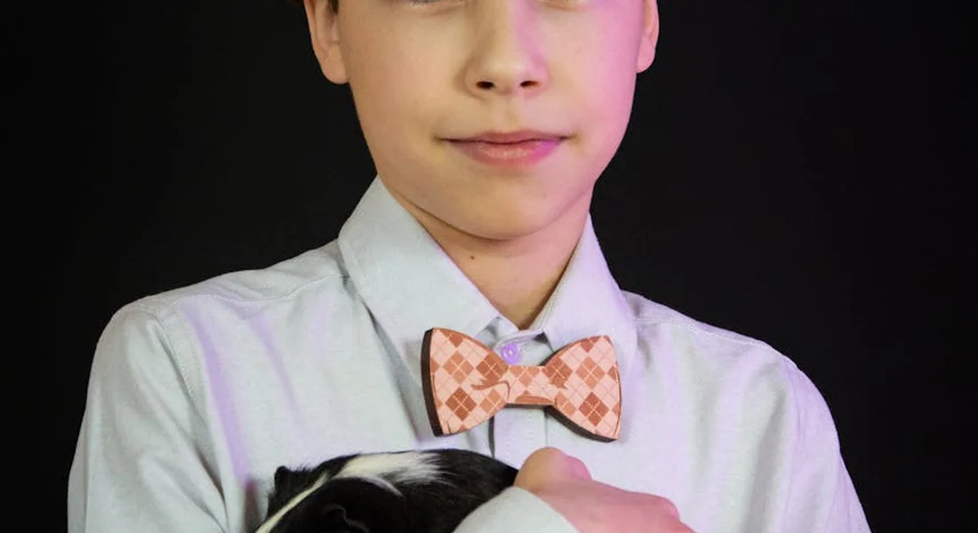 A person in a light shirt and peach checkered bow tie gently holding a guinea pig against a dark background.