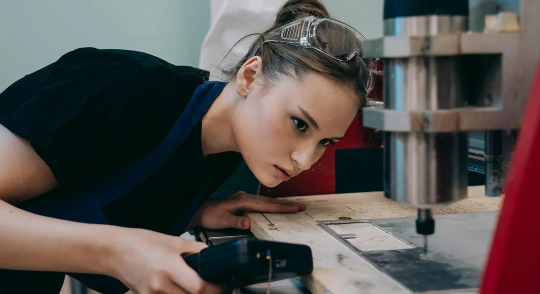 Person wearing protective safety goggles leaning toward a milling machine, illustrating eye protection in the workplace.