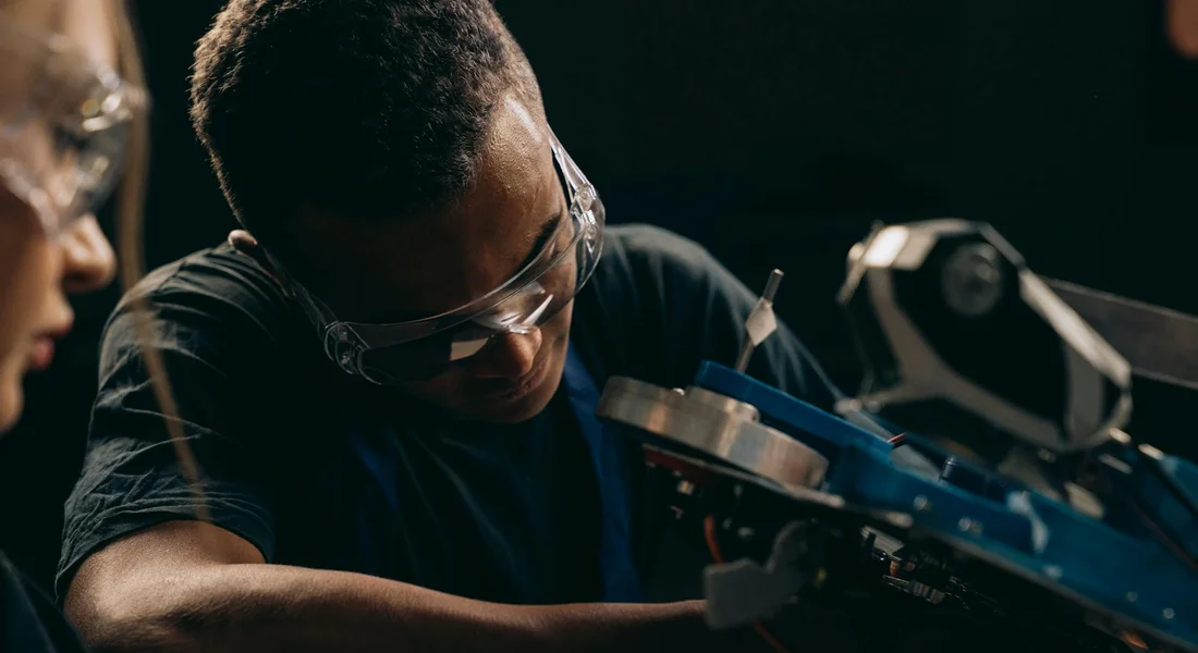 Two workers wearing safety goggles inspect machinery, emphasizing eye protection.
