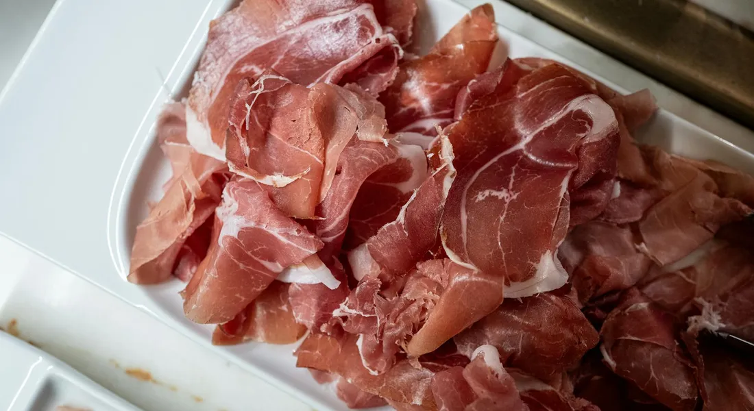 Thin slices of red cured ham arranged on a white plate.
