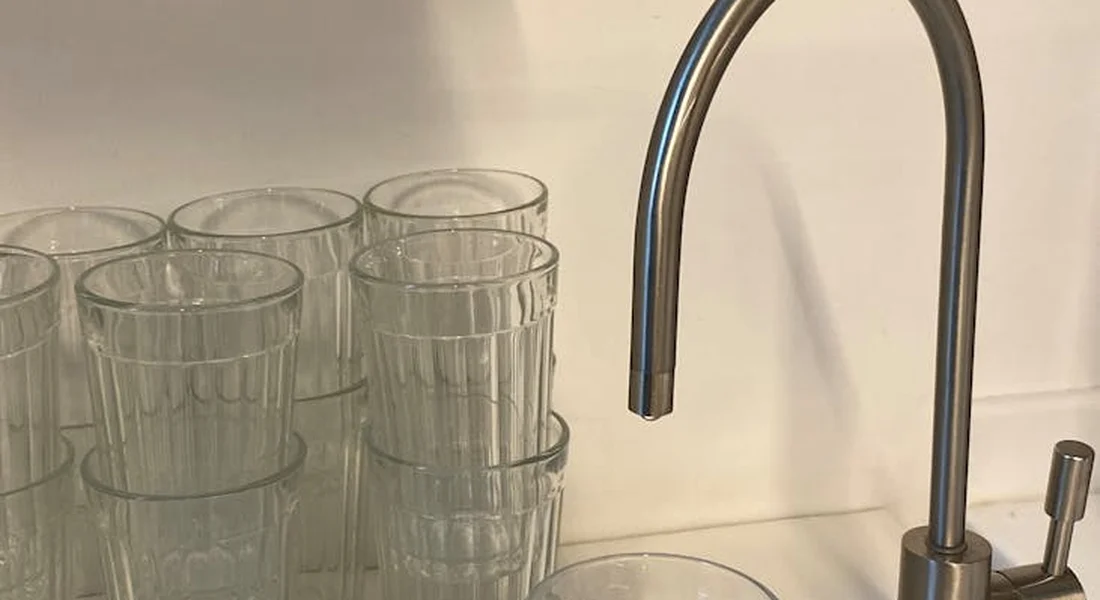 Clear glasses stacked on a counter beside a modern kitchen faucet, prepared for at-home water testing.