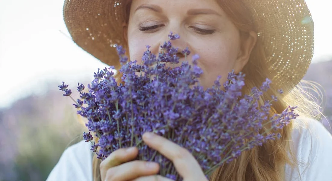 Woman wearing a straw hat smelling a bouquet of lavender