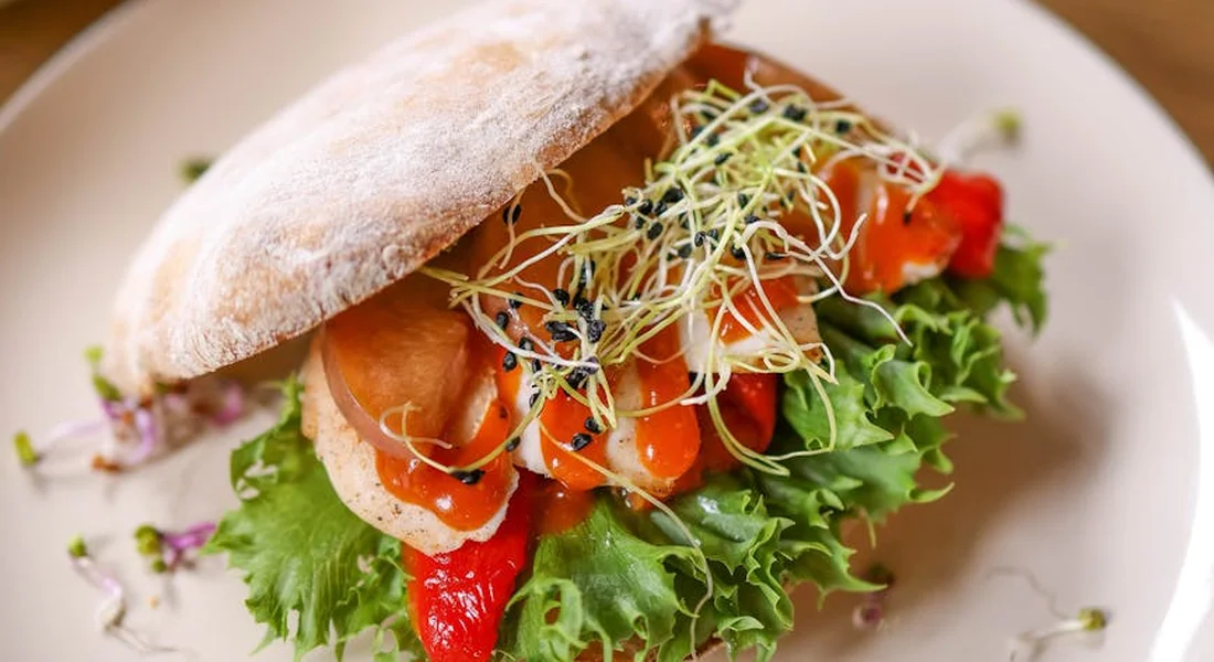 Sandwich on a plate topped with lettuce, tomato slices, and a handful of light sprouts (alfalfa) on top.